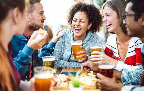 Diverse group of people smiling holding beers at a table.