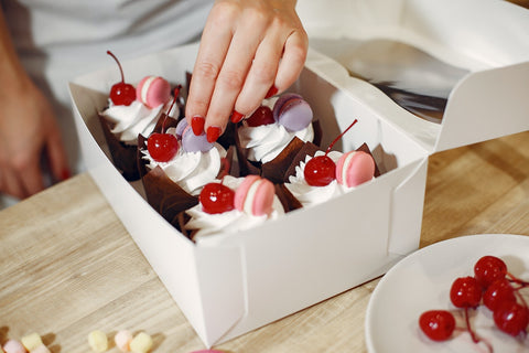 Hand putting macrons on top of cupcakes in a box.